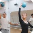 Two dancers practise in a mirrored studio, arms outstretched beneath hanging blue balls.