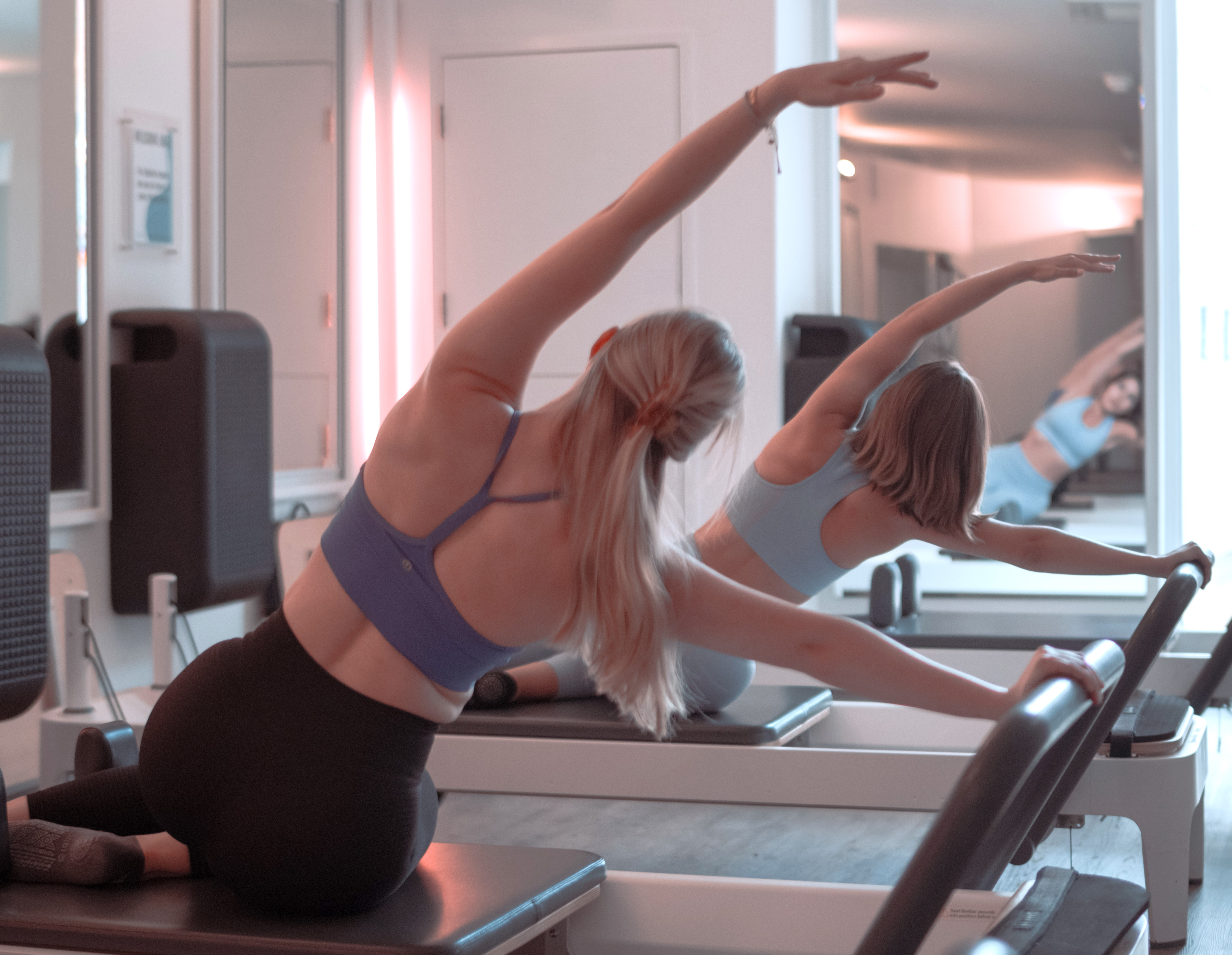 Two women exercising in a well-lit, modern Pilates Reformer studio.